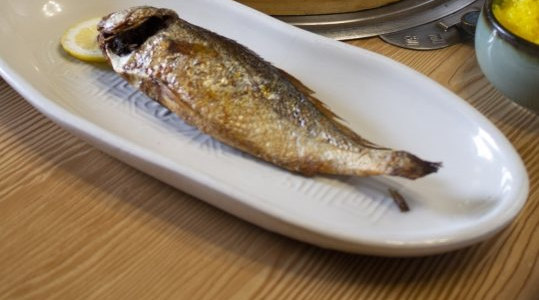 긴 흰 접시에 올린 통째 구운 생선 한 마리와 레몬 한 조각